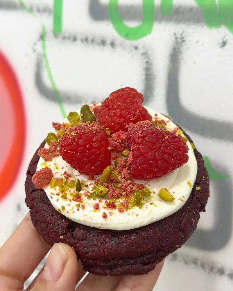 Cookie de red velvet con crema, frambuesas y pistacho, frente a la pared pintada con grafitis de la tienda